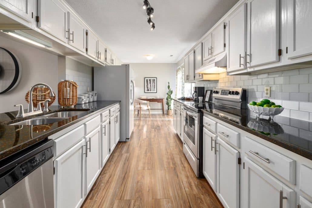Galley kitchen with white cabinets, dark granite counters and wood-look flooring