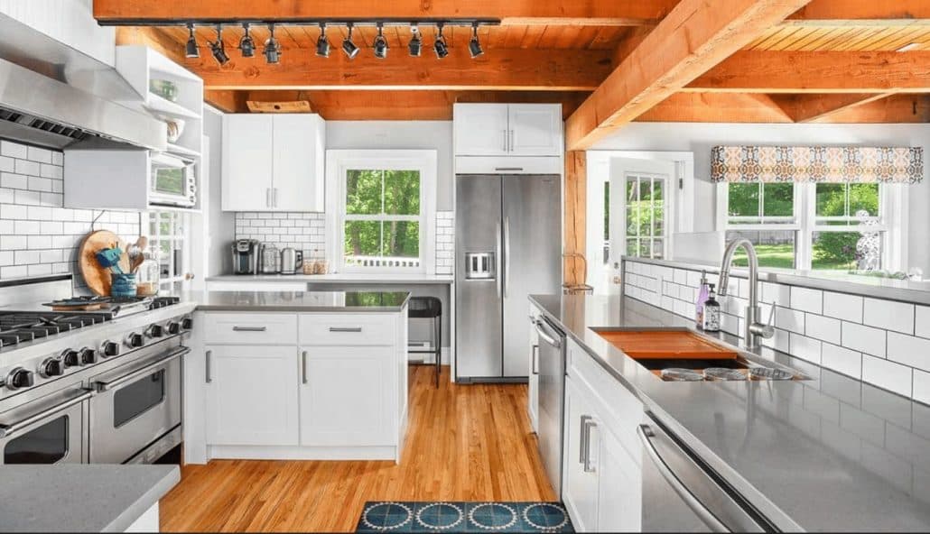 White shaker kitchen with exposed wood beams, stainless appliances and gray countertops