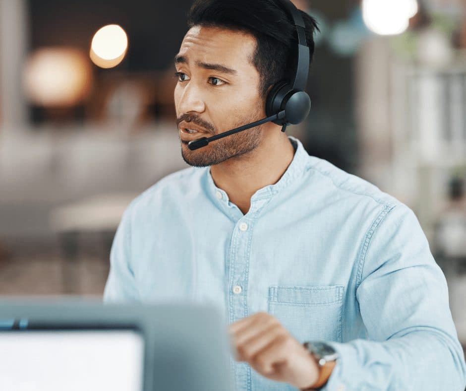 Man in a light blue shirt wearing a headset at a laptop